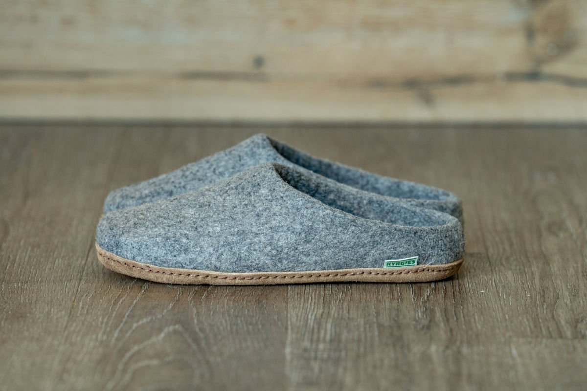 A grey wool-felt Kyrgies slipper resting on a warm wooden floor.